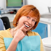 Senior woman in dental chair pointing to smile