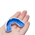 Hand holding blue and white mouthguard