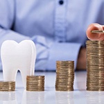 cost of dental implants in Huntington Beach represented by stacked coins and tooth