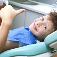 Smiling little boy in dental chair giving thumbs up