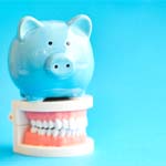 Piggy bank atop model teeth representing cost of dental emergencies in Huntington Beach