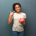 Woman holding piggy bank pointing to smile after toothache treatment in Huntington Beach