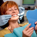 An older woman with red hair admires her smile in the mirror after receiving her dental implants in Huntington Beach