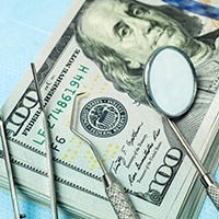 Money and dental tools representing cost of dental implants in Huntington Beach
