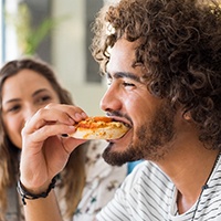 Male Invisalign patient enjoying delicious piece of pizza