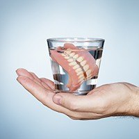 Hand holding dentures in glass of water