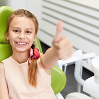 Young girl in dental chair giving a thumbs up