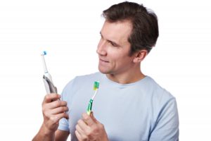 Man choosing between a manual and electric toothbrush