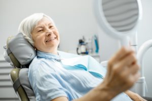 older woman admiring her dental implants in Huntington Beach in the mirror 