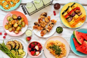 birds eye view of plates on a table containing assorted grilled meat, fruits, and vegetables