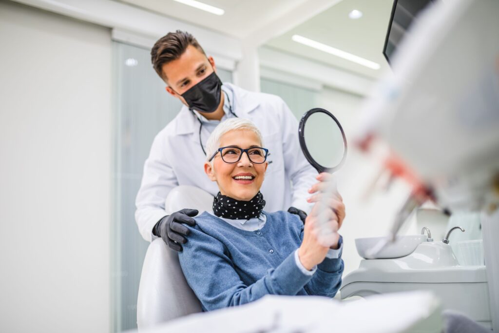 Dentist standing behind patient as she admires her smile in mirror