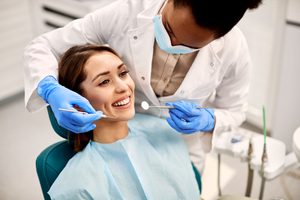 Woman in dental chair smiling as dentist leans in to examine her teeth
